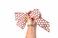 a hand holding onto a red and white bow with diamond pattern on the side, against a white background