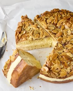 a sliced cake with almonds on top and one slice missing from it, next to a knife