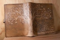 an open leather book with a tree on the front and back cover, sitting on top of a wooden shelf