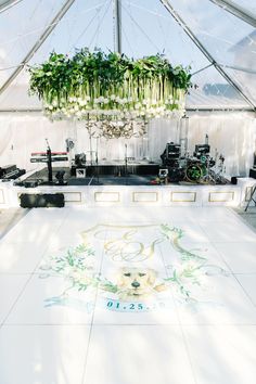 a white dance floor in a tent with plants hanging from it's ceiling and music equipment on the ground