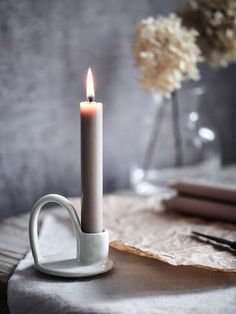 a lit candle sitting on top of a table next to a vase with flowers in it