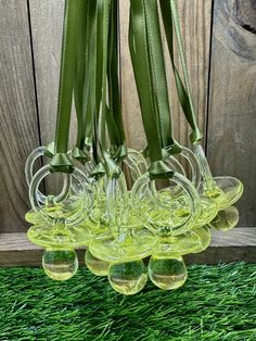 four glass vases with green ribbons hanging from them on the grass in front of a wooden fence