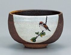 a small bowl with a bird painted on the side and green leaves in the bottom