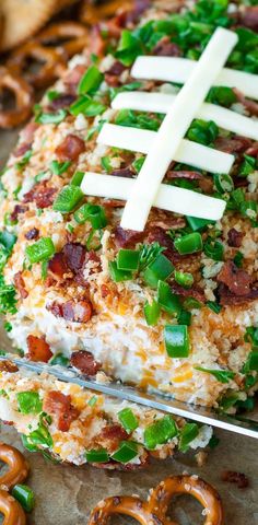 a football shaped pretzel with green onions and bacon on it, sitting next to pretzels