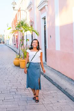 a woman walking down the street in front of a pink building with potted plants