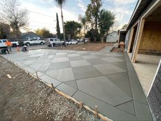 some construction workers are working on a concrete slab in the middle of a yard with cars parked behind it