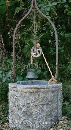 an old fashioned water fountain in the middle of some bushes and trees with vines around it