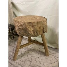 a wooden stool sitting on top of a rug next to a white sheet covered wall