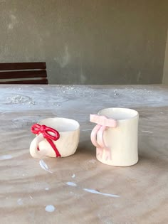 two mugs sitting on top of a table covered in wax paper and red ribbon