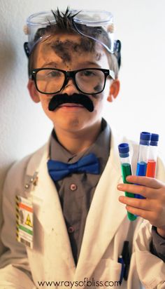 a young boy dressed as a scientist holding test tubes with colored liquids in them and wearing a fake moustache