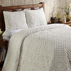 a bed with white bedspread and pillows in a rustic style bedroom, next to a wooden headboard