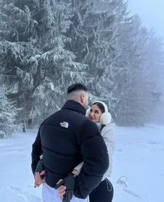 a man and woman standing in the snow with trees in the backgrouds