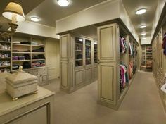 a walk in closet with lots of clothes on shelves and lights hanging from the ceiling