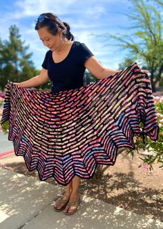 a woman is standing on the sidewalk holding a colorful shawl in her hands and looking down