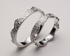 two silver rings with intricate designs on each side, set against a gray background and one is