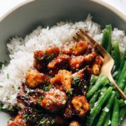 a white bowl filled with rice and green beans covered in sauce next to a fork