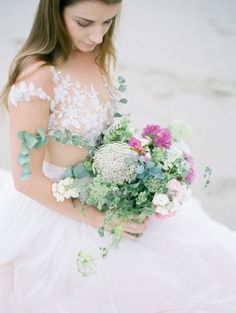 a woman in a white dress holding a bouquet of flowers and greenery on her shoulder