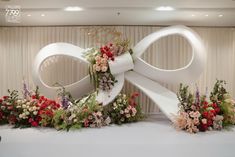 a large white bow decorated with flowers in front of a curtained wall behind it