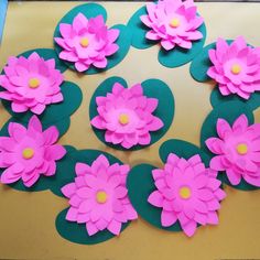 pink paper flowers are arranged in a circle on top of green leaves and yellow centers