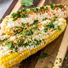 grilled corn on the cob topped with parsley and seasoning sitting on a cutting board