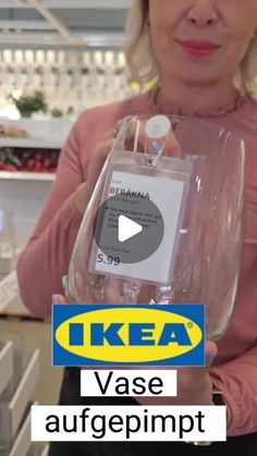 a woman is holding a clear wine glass in front of the camera and an ikea sign