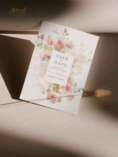 an elegant floral save the date card is displayed on top of a beige envelope with a feather