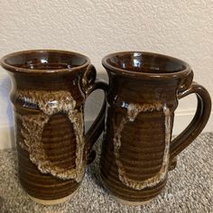 two brown coffee mugs sitting on top of a carpeted floor next to each other