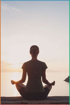 a woman sitting in a lotus position with the sun setting behind her