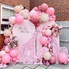 a pink and white backdrop with balloons, giraffes and flowers on it