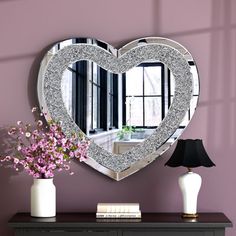 a heart shaped mirror sitting on top of a dresser next to a vase with flowers