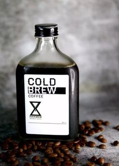 a bottle of cold brew coffee sitting on top of some coffee beans next to it