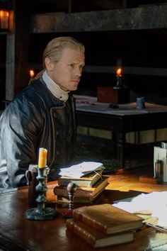 a man sitting at a table with books and candles