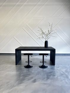 a table with two stools and a vase on it in front of a wall