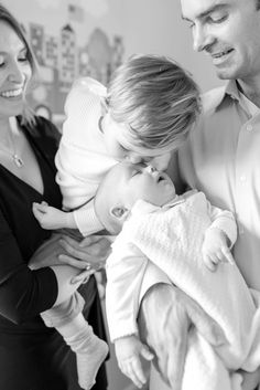 a man holding a baby in his arms while two women look at him and smile