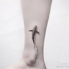 a shark tattoo on the ankle is shown in black and grey colors, with water droplets coming from its tail