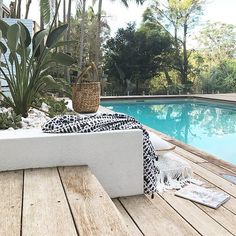 an outdoor table next to a pool with plants and towels on it in the foreground