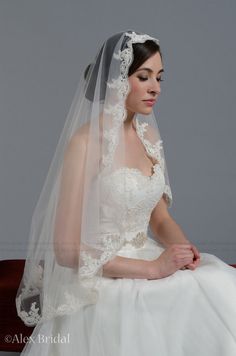 a woman wearing a wedding veil sitting on top of a wooden table in front of a gray background