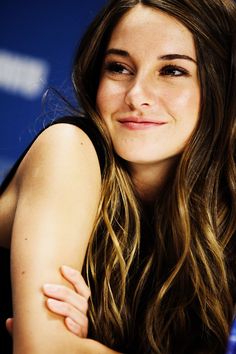 a woman with long hair sitting in front of a blue wall and smiling at the camera