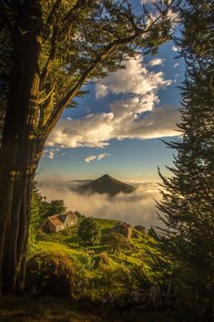 the sun is shining through the clouds over some trees and houses on a hill with mountains in the distance