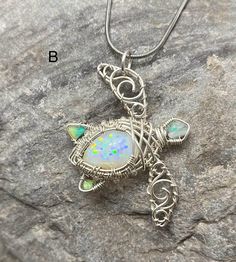 a silver necklace with an opal stone in the center on top of a rock