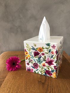 a tissue box sitting on top of a wooden table next to a pink and yellow flower