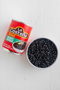 a can of black beans next to a white bowl filled with it's contents