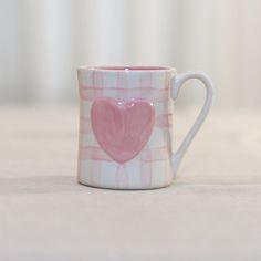 a pink and white checkered coffee cup with a heart painted on the inside of it