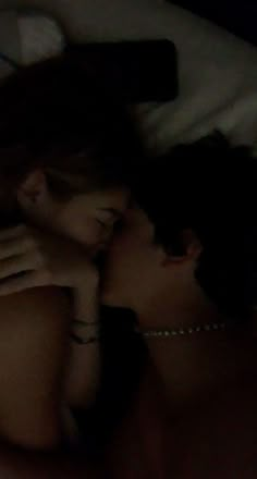 two people are laying in bed and one is kissing the other's foreheads