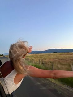 a woman is waving out the window of a car while driving down a country road