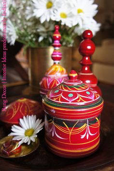 colorfully painted pots and containers on a table with daisies in the foreground