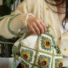 a woman is holding a crocheted purse with flowers on the front and sides