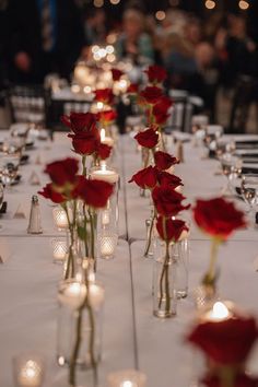 several vases filled with red roses on top of a long table covered in candles