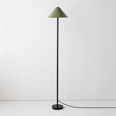 a black floor lamp with a green shade on the base and a white wall behind it