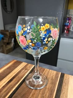 a wine glass with flowers painted on it sitting on a wooden table in a kitchen